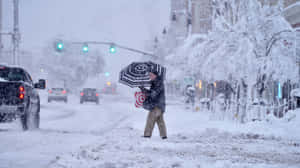 在冬季風暴中撐傘穿過積雪街道的人。 — 冬季 壁紙
