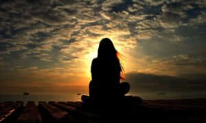 日落時分，在碼頭上冥想的人，背景是戲劇性的雲層和海洋 — 暗黑少女風 壁紙