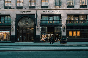 黃昏時分，一個人在城市街道上走過奢侈品品牌店鋪。 — Burberry 壁紙