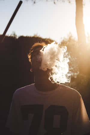 一個人在日落時呼出蒸氣，身後有剪影樹木。 — 抽菸 壁紙