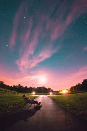 人坐在小路的椅子上，在星空下，有粉紅色和藍綠色的雲 — 美學粉色GIF 壁紙