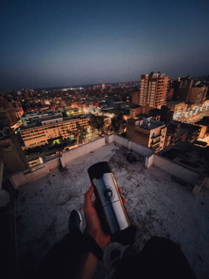 手在天台上拿著保溫瓶俯瞰城市 — 夜景城市 壁紙
