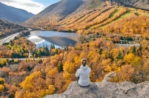 一個人坐在岩石上，俯瞰秋葉中的湖泊。 — 登山 壁紙