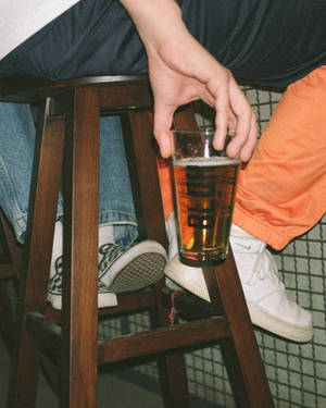 坐在木凳上手持啤酒杯的人，穿著牛仔褲和運動鞋。 — 酒吧 壁紙