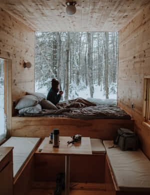 人坐在木屋床上透過窗戶看雪森林 — 冬季風景 壁紙