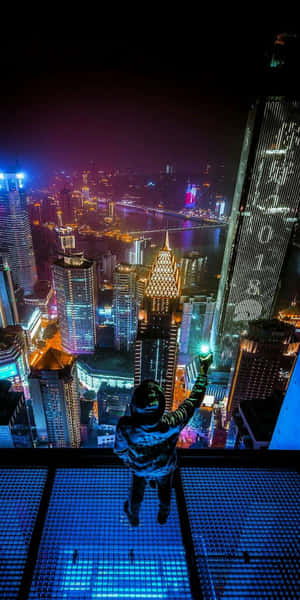 玻璃陽台上的人俯瞰夜晚發光的城市 — Pixel 3 壁紙