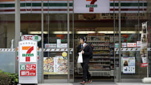 一個人戴著耳機走過一間有日文招牌的7-Eleven便利商店。 — 7-ELEVEN 壁紙