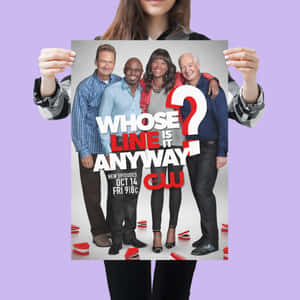 一個人手持《Whose Line Is It Anyway?》電視節目海報，海報上有四位微笑的演員。 — 演員 壁紙