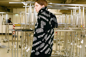 在金屬欄杆倉庫中佩戴品牌圍巾的人。 — Vetements 壁紙