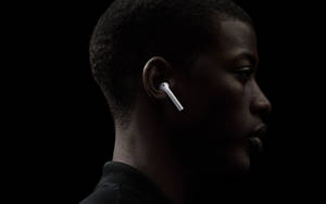 在暗色側面照中戴著白色無線耳機的人 — AirPods 壁紙