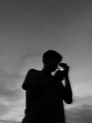 一個人在陰雲密佈的黃昏天空下點燃香煙的剪影。 — 抽菸 壁紙
