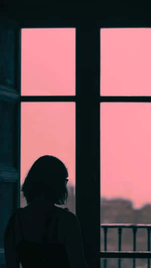 剪影人物望向窗外，看著粉紅色日落。 — 옥자 壁紙