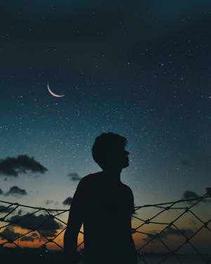 一個人透過鐵絲網仰望彎月和星星的剪影。 — 螢幕 壁紙