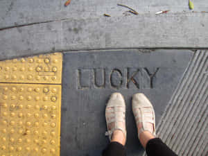 穿著米色涼鞋的腳站在刻有LUCKY的人行道上。 — 好運 壁紙