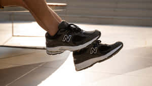 特寫鏡頭：黑色New Balance運動鞋中的腳懸浮在陽光照射的路面上方。 — New Balance 壁紙