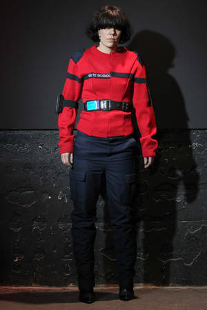 穿著紅黑時尚服裝的人站在深色紋理牆前。 — Vetements 壁紙