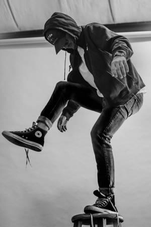 穿著連帽衫和牛仔褲的人平衡在凳子上，一隻腳抬起。 — Converse 壁紙