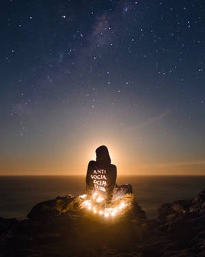 夜晚坐在懸崖上，在星空下手持發光燈光的人