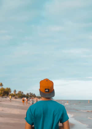 戴橙色帽子和青綠色襯衫的人在海灘上行走，靠近海洋 — 海灘度假 壁紙