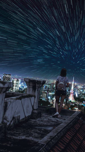 人在屋頂上凝視著夜間燈火通明的城市上空的星軌 — 城市燈光 壁紙