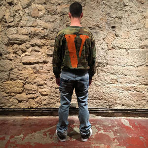 穿著迷彩連帽衫和破洞牛仔褲的人站在石牆前。 — Vlone 壁紙