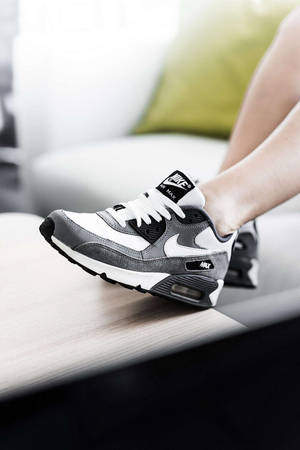 一個人腳部穿著灰色和白色的Nike Air Max運動鞋在木質表面上。