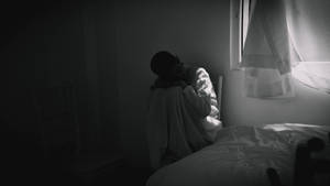 一個人裹著毯子，蜷縮在昏暗房間的窗邊。 — 孤獨 壁紙