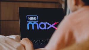 躺在床上用筆記型電腦觀看HBO Max的人。 — HBO 壁紙