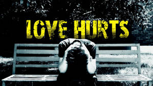坐在長椅上，在 'LOVE HURTS' 字樣下低着頭的人。 — 心碎 壁紙
