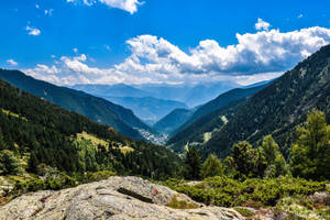 山谷的全景，森林覆蓋的山坡和下方的小鎮，在晴朗的藍天下。 — 山景 壁紙