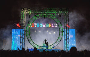 在帶有「ASTROWORLD」標誌的發光綠色圓形舞台下，夜間音樂會的剪影人群。 — 崔維斯·史考特 天文世界 壁紙