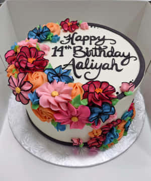 一個生日蛋糕，上面有色彩繽紛的花朵和黑色糖霜寫的「Happy 14th Birthday Aaliyah」。 — Pixel Fold 壁紙