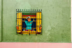 一個穿著藍綠色服裝的稻草人掛在帶黃色百葉窗的鐵欄杆窗戶上。 — 布宜諾斯艾利斯 壁紙
