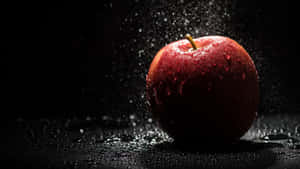 一個紅蘋果在黑色表面上周圍有水珠濺起。 — 4K Apple 壁紙