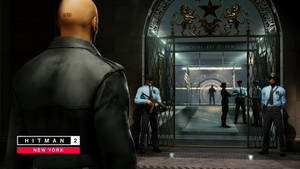 特工47站在《Hitman 2 New York》中一個有守衛的建築物入口前。 — iMac 壁紙