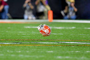 克萊姆森美式足球頭盔在燈光球場上，背景有模糊的攝影師。 — 大學美式足球 壁紙