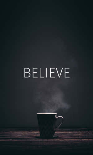 一個冒煙的馬克杯，上方有「BELIEVE」字樣，置於木質表面。 — Tecno Megapad 壁紙