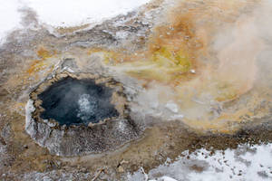一個冒著蒸汽的地熱池，在白雪皚皚的冬季景觀中，帶有色彩繽紛的礦物沉積物。 — 黃石國家公園 壁紙