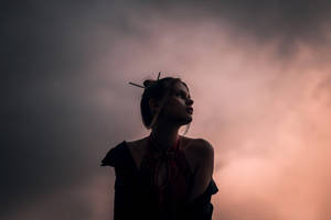 剪影中的女人看著帶有粉紅色和灰色雲彩的黃昏天空。 — 美學天空 壁紙