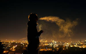 人物在夜晚發光的城市上空呼出煙霧。 — 抽菸 壁紙