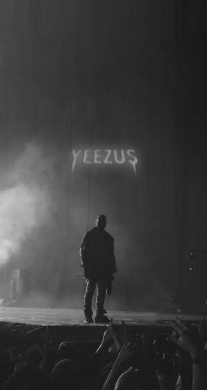 剪影表演者在舞台上，上方有「YEEZUS」標誌，下方群眾伸手向上。 — 肯伊·威斯特 壁紙