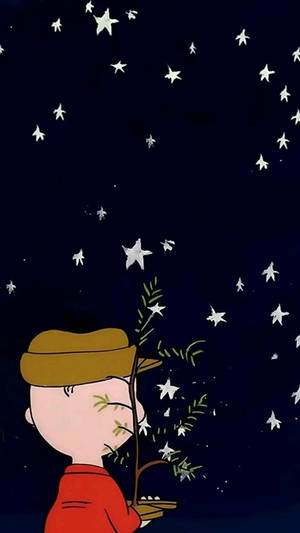 一個身穿紅色襯衫和棕色帽子的男孩，在星空下拿著一棵小樹。 — 史努比聖誕節 壁紙