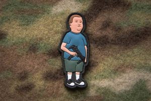 卡通補丁，一個男孩在迷彩布上拿著步槍。 — 巴比·希爾 壁紙