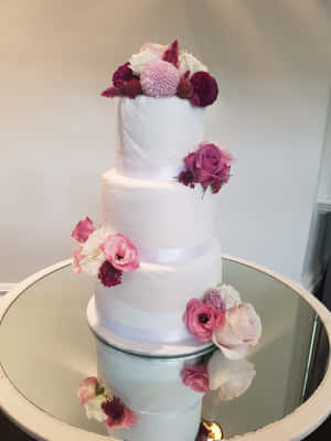 四層白色結婚蛋糕，以粉紅色和酒紅色花朵裝飾，擺放在鏡面桌上。 — iPad 第9代 壁紙