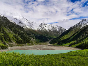 一個山谷中的碧綠湖泊，有積雪的山峰和翠綠的山坡。 — 山脈 壁紙