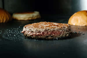 一個多汁的漢堡肉餅在黑色烤盤上烹調，周圍有麵包。 — 薯條 壁紙