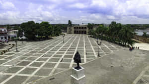 一個大型瓷磚廣場，中央有雕像和歷史建築，天空多雲。 — 皇帝佐格 壁紙