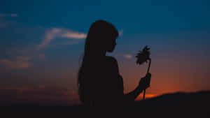 女人在日落時手持向日葵，剪影映襯著色彩繽紛的天空 — 女孩 壁紙
