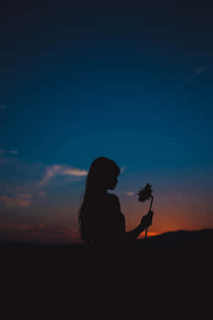 女人在暮色中手持花朵，以色彩繽紛的天空為背景。 — 剪影 壁紙