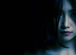 一個女人的臉部在昏暗的藍光中，背景黑暗，表情嚴肅。 — 暗黑少女風 壁紙